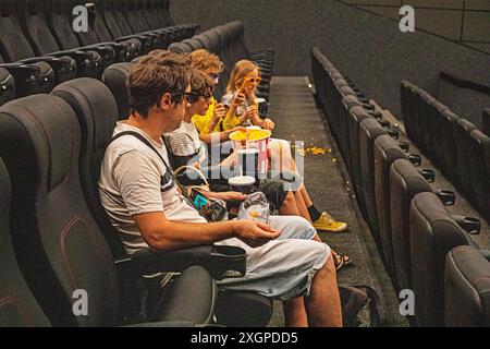 Kinder und Papa sitzen in der Kinohalle, tragen eine 3D-Brille mit Popcorn und einem Drink, bevor sie zusehen. Familienwochenende Stockfoto