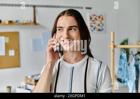 Ein junger schwuler Mann, Besitzer eines Heimwerkerateliers, lächelt, während er telefoniert. Stockfoto