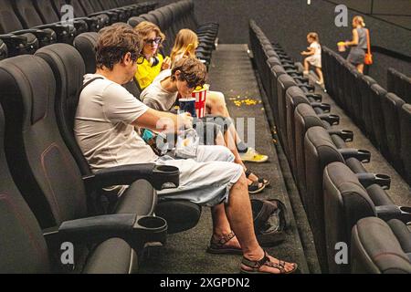 Kinder und Papa sitzen in der Kinohalle, tragen eine 3D-Brille mit Popcorn und einem Drink, bevor sie zusehen. Familienwochenende Stockfoto