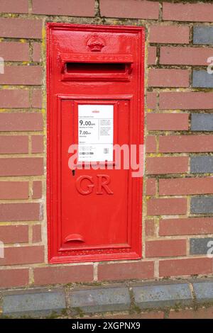 Nahaufnahme eines roten Briefkastens von Royal Mail mit den königlichen Verschlüsselungsbuchstaben GR auf der Vorderseite, in einer traditionellen Backsteinmauer im Freien, Großbritannien. Stockfoto