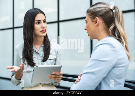 Zwei Kollegen, die ein digitales Tablet verwenden und im Freien sprechen. Moderne Geschäftskollegen unterhalten sich vor dem Bürogebäude auf t Stockfoto
