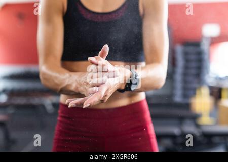 Eine fitte junge kaukasische Frau bereitet sich auf ein Training im Fitnessstudio vor. Kreidestaub fliegt, während sie ihre Hände zusammenklatscht, bereit für Gewichtheben oder Gymnastik. Stockfoto