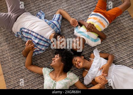 Vielfältige Familie genießt eine angenehme Zeit zu Hause. Sie teilen einen fröhlichen Moment, auf dem Boden liegen und eine enge Bindung schaffen. Stockfoto