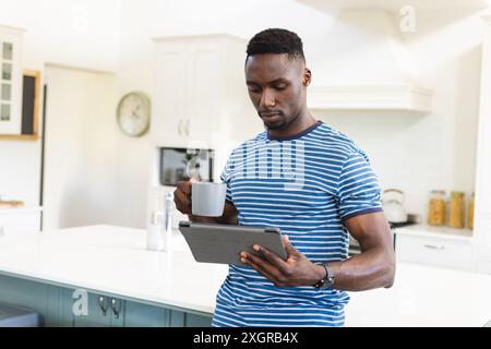 Fokussierter afroamerikanischer Mann, der Kaffee trinkt und ein Tablet benutzt, das in der sonnigen Küche steht, Kopierraum. Kommunikation, Erfrischung, Morgen, häusliches Leben Stockfoto