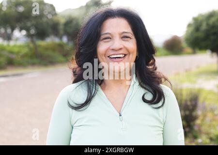 Porträt einer glücklichen älteren Frau mit langen schwarzen Haaren, die draußen lächelt. Wohlbefinden, Gesundheit und aktiver Lebensstil der Senioren, unverändert. Stockfoto