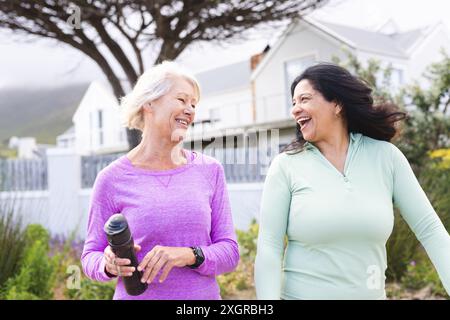 Zwei glückliche ältere Freundinnen gehen zum Sport auf der Landstraße und unterhalten sich. Freundschaft, Fitness, Bewegung, Aktivität und gesunde Senioren l Stockfoto