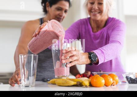 Glückliche ältere Freundinnen, die Obst-Smoothie in die Küche gießen. Essen, Ernährung, Freundschaft, häusliches Leben und gesunde Seniorenleben, unalte Stockfoto