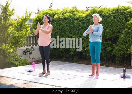 Zwei glückliche ältere Freundinnen üben Yoga Meditation, stehend im sonnigen Garten. Yoga, Wohlbefinden, Meditation, Freundschaft und gesundes senio Stockfoto