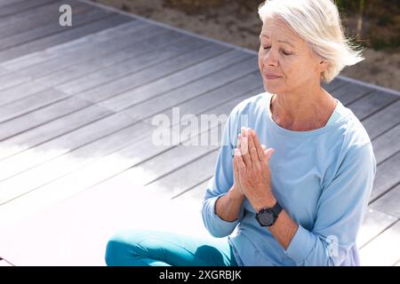 Kaukasische ältere kaukasische ältere Frau praktiziert Yoga-Meditation im sonnigen Garten. Yoga, Wohlbefinden, Meditation, Freundschaft und gesunde Senioren Stockfoto