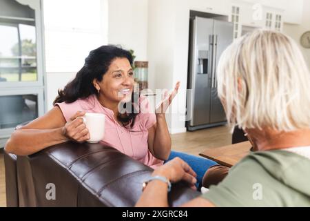 Zwei glückliche ältere Freundinnen, die Kaffee trinken und sich unterhalten, sitzen auf dem Sofa im Wohnzimmer. Freundschaft, Entspannung, Ruhestand, häusliches Leben und Stockfoto