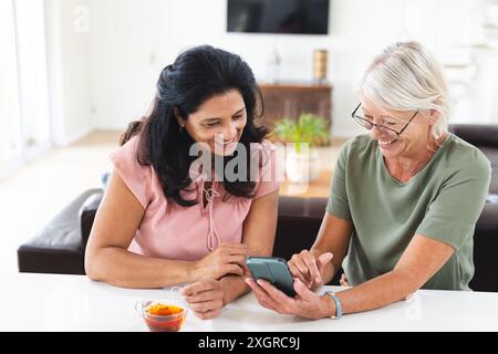 Zwei glückliche ältere Freundinnen, die ihr Smartphone benutzen und in der Küche sprechen. Freundschaft, Kommunikation, Entspannung, Ruhestand, häusliches Leben und Stockfoto