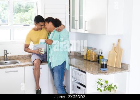 Schwules birassisches Paar, das einen Moment in einer hellen Küche teilt. Sie genießen einen gemütlichen gemeinsamen Morgen mit Wärme und Zuneigung. Stockfoto