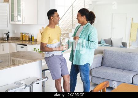 Ein Mann aus dem Nahen Osten und ein junger birassischer Mann, ein schwules Paar, das in einer hellen Küche plaudert. Sie teilen sich einen entspannten Moment mit Kaffee und reflektieren einen Comf Stockfoto