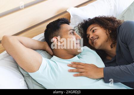 Birassisches Paar genießt einen entspannten Moment zu Hause, mit Kopierraum. Sie teilen eine enge und liebevolle Verbindung, während sie auf dem Bett liegen. Stockfoto
