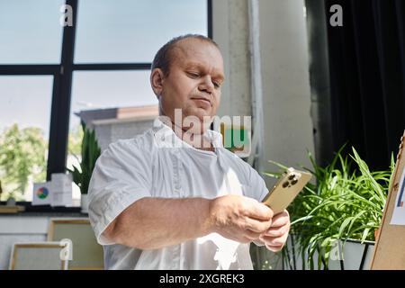 Ein Mann mit Inklusivität, der ein weißes Hemd trägt, benutzt sein Handy in einem sonnendurchfluteten Büro. Stockfoto