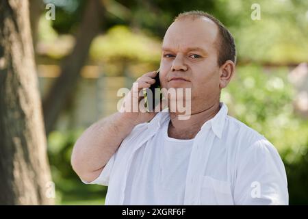 Ein Mann mit Inklusivität spaziert durch einen Park und spricht an einem sonnigen Tag mit seinem Telefon. Stockfoto