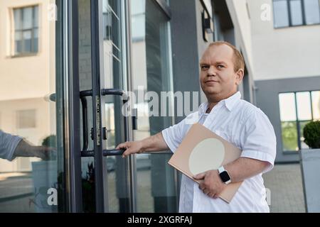 Ein Mann mit Inklusivität verlässt ein Gebäude, hält eine Mappe und trägt ein weißes Hemd. Stockfoto