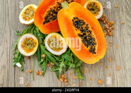 Papaya-Frucht, Passionsfrucht, Rucola und Müsli auf hellem hölzernem Hintergrund. Scheiben süßer Papaya, Maracuja, grüner Rucola umgeben von Granola fla Stockfoto