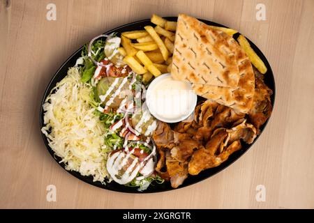 Ein köstlicher Teller gemischter Döner-Döner mit Salat, Pommes, Pita-Brot und Sauce auf einem Holztisch Stockfoto