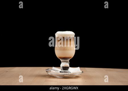 Ein wunderschön geschichteter Latte Macchiato in einem Glas auf einem Holztisch vor schwarzem Hintergrund Stockfoto