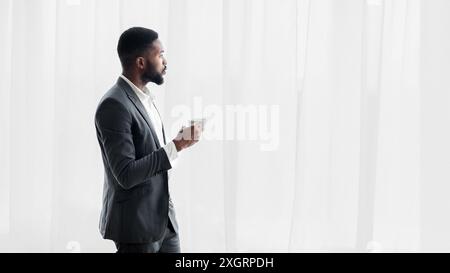 Nachdenklicher schwarzer Geschäftsmann, der aus dem Fenster blickt und Kaffee trinkt Stockfoto