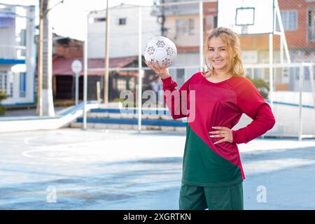 Konzepte: Sport und Freizeit im Freien. Die schöne Fußballspielerin lächelt, während sie einen Ball in der Hand hält und bereit ist, mit dem Training zu beginnen. Aktiv und aktiv Stockfoto