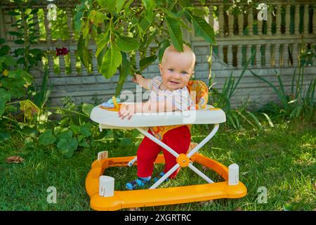 Baby Mädchen im Garten in einem Wanderer lernt zu gehen, die ersten Schritte in einem Wanderer Stockfoto