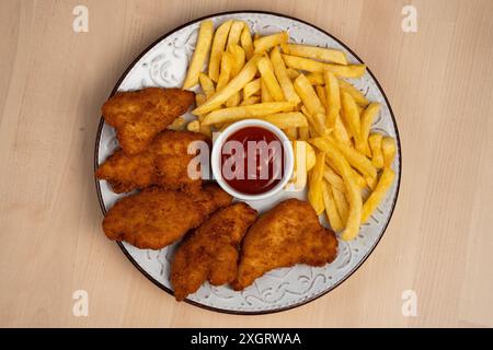 Ein Blick von oben auf den Teller mit knusprigen gebratenen Hähnchenflügeln mit Pommes frites und einer Seite Ketchup auf einem Holztisch Stockfoto
