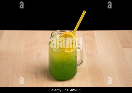 Eine erfrischende grüne Limonade in einem maurerglas mit gelbem Strohhalm und Zitronenscheibe auf einem Holztisch Stockfoto