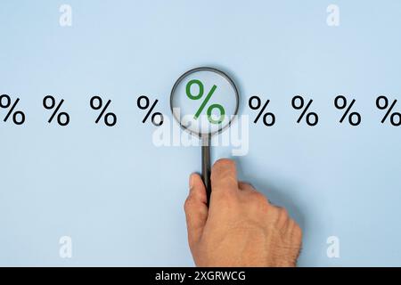 Nahaufnahme einer Hand, die eine Lupe über einem Prozentzeichen auf blauem Hintergrund hält. Fokus, Analyse und Inspektionskonzept. Stockfoto
