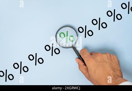 Nahaufnahme einer Hand, die eine Lupe über einem Prozentzeichen auf blauem Hintergrund hält. Fokus, Analyse und Inspektionskonzept. Stockfoto