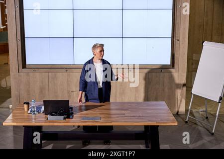 Weibliche Sprecherin in formeller Kleidung hält Vortrag auf Geschäftskonferenzen. Nette weiße Moderatorin benutzt Präsentationsbildschirm. Unternehmensleitung Stockfoto