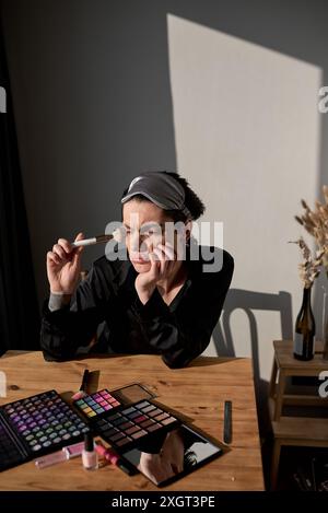 Porträt eines jungen Transgenders in schwarzem Gewand, der sich auf seinen Ellenbogen stützt und mit der Hand auf der Wange seitlich schaut, Nahaufnahme Porträt. Negatives Emotopn Stockfoto