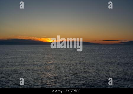 Ein kleines einsames Fischerboot segelt über das ruhige Wasser des Skagerrak-Meeres, wobei die aufgehende Sonne in der Nähe der Küste Norwegens goldene Schimmer am Horizont strahlt Stockfoto