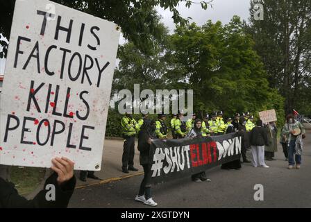 Leicester, Leicestershire, Großbritannien. Juli 2024. Ein Demonstrant hält ein Schild mit der Aufschrift „˜diese Fabrik tötet Menschen“ hoch, während andere Demonstranten den Eingang zur Fabrik während der Demonstration blockieren. Demonstranten versammeln sich vor den Toren der Fabrik von Elbit System in Leicester, um zu protestieren, während Arbeiter bei der israelischen Rüstungsfirma arbeiten. Die Demonstranten protestieren gegen die Waffen, die in dieser Fabrik hergestellt wurden, die ihrer Meinung nach später zur Unterdrückung der Palästinenser in Gaza und anderswo eingesetzt werden. 85 % der israelischen Drohnenflotte werden von Elbit Systems beliefert und die Demonstranten wollen ihre sieben verbleibenden Geschäfte Stockfoto