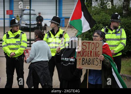 Leicester, Leicestershire, Großbritannien. Juli 2024. Ein Demonstrant hält ein Schild mit der Aufschrift „hört auf, Babys zu ermorden“, während ein anderer während der Demonstration am Eingang der Fabrik eine palästinensische Flagge schwingt. Demonstranten versammeln sich vor den Toren der Fabrik von Elbit System in Leicester, um zu protestieren, während Arbeiter bei der israelischen Rüstungsfirma arbeiten. Die Demonstranten protestieren gegen die Waffen, die in dieser Fabrik hergestellt wurden, die ihrer Meinung nach später zur Unterdrückung der Palästinenser in Gaza und anderswo eingesetzt werden. 85 % der israelischen Drohnenflotte werden von Elbit Systems beliefert und die Demonstranten wollen ihre sieben verbleibenden Busine Stockfoto