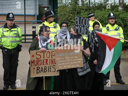 Leicester, Leicestershire, Großbritannien. Juli 2024. Polizeibeamte bilden am Eingang der Fabrik eine Absperrung, während Demonstranten während der Demonstration Schilder gegen Elbit Systems halten. Demonstranten versammeln sich vor den Toren der Fabrik von Elbit System in Leicester, um zu protestieren, während Arbeiter bei der israelischen Rüstungsfirma arbeiten. Die Demonstranten protestieren gegen die Waffen, die in dieser Fabrik hergestellt wurden, die ihrer Meinung nach später zur Unterdrückung der Palästinenser in Gaza und anderswo eingesetzt werden. 85 % der israelischen Drohnenflotte werden von Elbit Systems beliefert, und die Demonstranten wollen, dass ihre sieben verbleibenden Unternehmen geschlossen werden Stockfoto