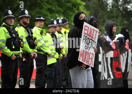 Leicester, Leicestershire, Großbritannien. Juli 2024. Polizeibeamte bilden am Eingang der Fabrik eine Absperrung, während Demonstranten während der Demonstration Schilder gegen Elbit Systems halten. Demonstranten versammeln sich vor den Toren der Fabrik von Elbit System in Leicester, um zu protestieren, während Arbeiter bei der israelischen Rüstungsfirma arbeiten. Die Demonstranten protestieren gegen die Waffen, die in dieser Fabrik hergestellt wurden, die ihrer Meinung nach später zur Unterdrückung der Palästinenser in Gaza und anderswo eingesetzt werden. 85 % der israelischen Drohnenflotte werden von Elbit Systems beliefert, und die Demonstranten wollen, dass ihre sieben verbleibenden Unternehmen geschlossen werden Stockfoto