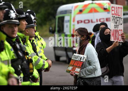 Leicester, Leicestershire, Großbritannien. Juli 2024. Polizeibeamte bilden am Eingang der Fabrik eine Absperrung, während Demonstranten während der Demonstration Schilder gegen Elbit Systems halten. Demonstranten versammeln sich vor den Toren der Fabrik von Elbit System in Leicester, um zu protestieren, während Arbeiter bei der israelischen Rüstungsfirma arbeiten. Die Demonstranten protestieren gegen die Waffen, die in dieser Fabrik hergestellt wurden, die ihrer Meinung nach später zur Unterdrückung der Palästinenser in Gaza und anderswo eingesetzt werden. 85 % der israelischen Drohnenflotte werden von Elbit Systems beliefert, und die Demonstranten wollen, dass ihre sieben verbleibenden Unternehmen geschlossen werden Stockfoto