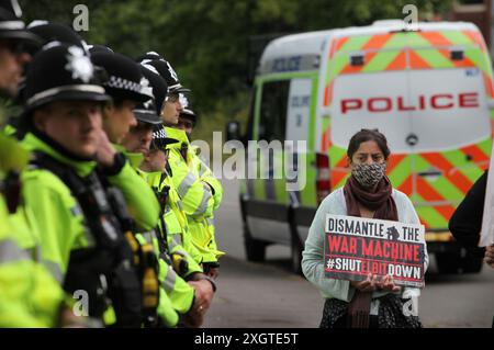 Leicester, Leicestershire, Großbritannien. Juli 2024. Polizeibeamte bilden am Eingang der Fabrik eine Absperrung, während Demonstranten während der Demonstration Schilder gegen Elbit Systems halten. Demonstranten versammeln sich vor den Toren der Fabrik von Elbit System in Leicester, um zu protestieren, während Arbeiter bei der israelischen Rüstungsfirma arbeiten. Die Demonstranten protestieren gegen die Waffen, die in dieser Fabrik hergestellt wurden, die ihrer Meinung nach später zur Unterdrückung der Palästinenser in Gaza und anderswo eingesetzt werden. 85 % der israelischen Drohnenflotte werden von Elbit Systems beliefert, und die Demonstranten wollen, dass ihre sieben verbleibenden Unternehmen geschlossen werden Stockfoto