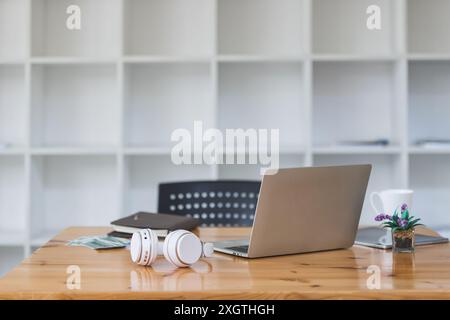 Laptop, Kopfhörer, Blumentopf, Geld usw. auf dem Schreibtisch im Heimbüro. Arbeitsbereich mit Laptop- und Bürobedarf. Stockfoto