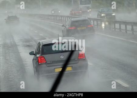 In der britischen Presse wurde häufig über das unsaisonale nasse Sommerwetter Mitte Juni und Anfang Juli 2024 berichtet. Passagiere einer Busreise im Sommer konnten diese sintflutartigen Regenfälle auf der Autobahn M4 beobachten, die von der oberen Ebene aus durch die Windschutzscheibe gesehen wurden. Der Fahrer auf der unteren Ebene ist auf Scheibenwischer angewiesen. Der obere Teil hier bietet gute Sicht auf das VW-Auto bei Regen und Nebel auf der Autobahn. Stockfoto