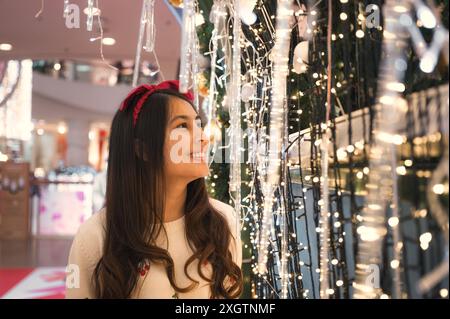 Attraktive junge asiatische Frau, die auf dem weihnachtsfest im Glühbirnentunnel-Dekor genießt Stockfoto