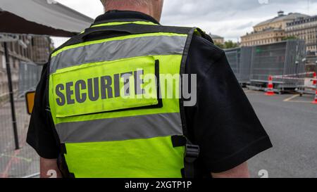 Fluoreszierende gelbe Weste mit dem Wort „Security“ auf der Rückseite, die von einem privaten Sicherheitsbeamten getragen wird, der einen sicheren Ort beobachtet Stockfoto