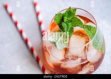 Nahaufnahme eines gekühlten Coca-Cola-Cocktails, garniert mit frischen Minzblättern in einem Glas, begleitet von rot-weiß gestreiften Strohhalmen, die gegen einen stehen Stockfoto