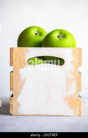 Reife grüne Äpfel werden ordentlich in einer rustikalen Holzkiste mit einem hellen weißen Hintergrund platziert, die ihre lebendige Farbe und Frische unterstreicht Stockfoto