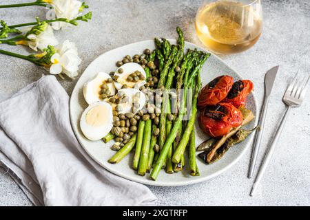 Eine nahrhafte Mahlzeit mit einem gekochten Ei, BBQ-Spargel, Kapern und gegrilltem Gemüse einschließlich Tomaten und Chili-Paprika, stilvoll auf einem präsentiert Stockfoto