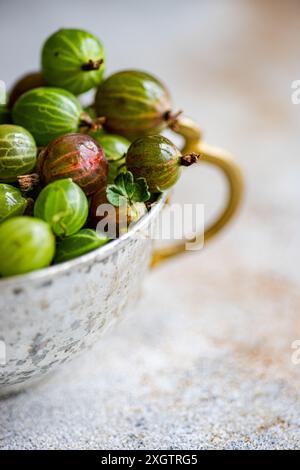 Nahaufnahme frischer Bio-Stachelbeeren in einem rustikalen, angetriebenen Metallbecher vor weichem Hintergrund. Die leuchtenden Grün- und Rottöne der Be Stockfoto