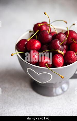 Von oben saftige rote Kirschen in einer bezaubernden Keramikschale mit Herzmotiven vor einem weichen grauen Hintergrund. Das leuchtende Rot der Kirschen steht im Kontrast Stockfoto
