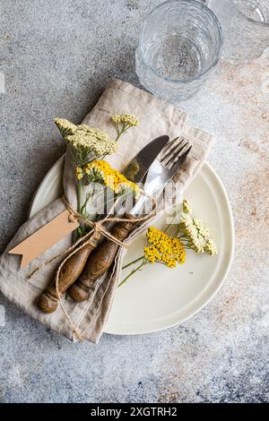 Ein Tisch im Vintage-Stil mit frischen wilden achillea-Blumen, sorgfältig mit rustikalem Besteck arrangiert, in eine Serviette und Krawatte aus natürlichem Leinen gewickelt Stockfoto